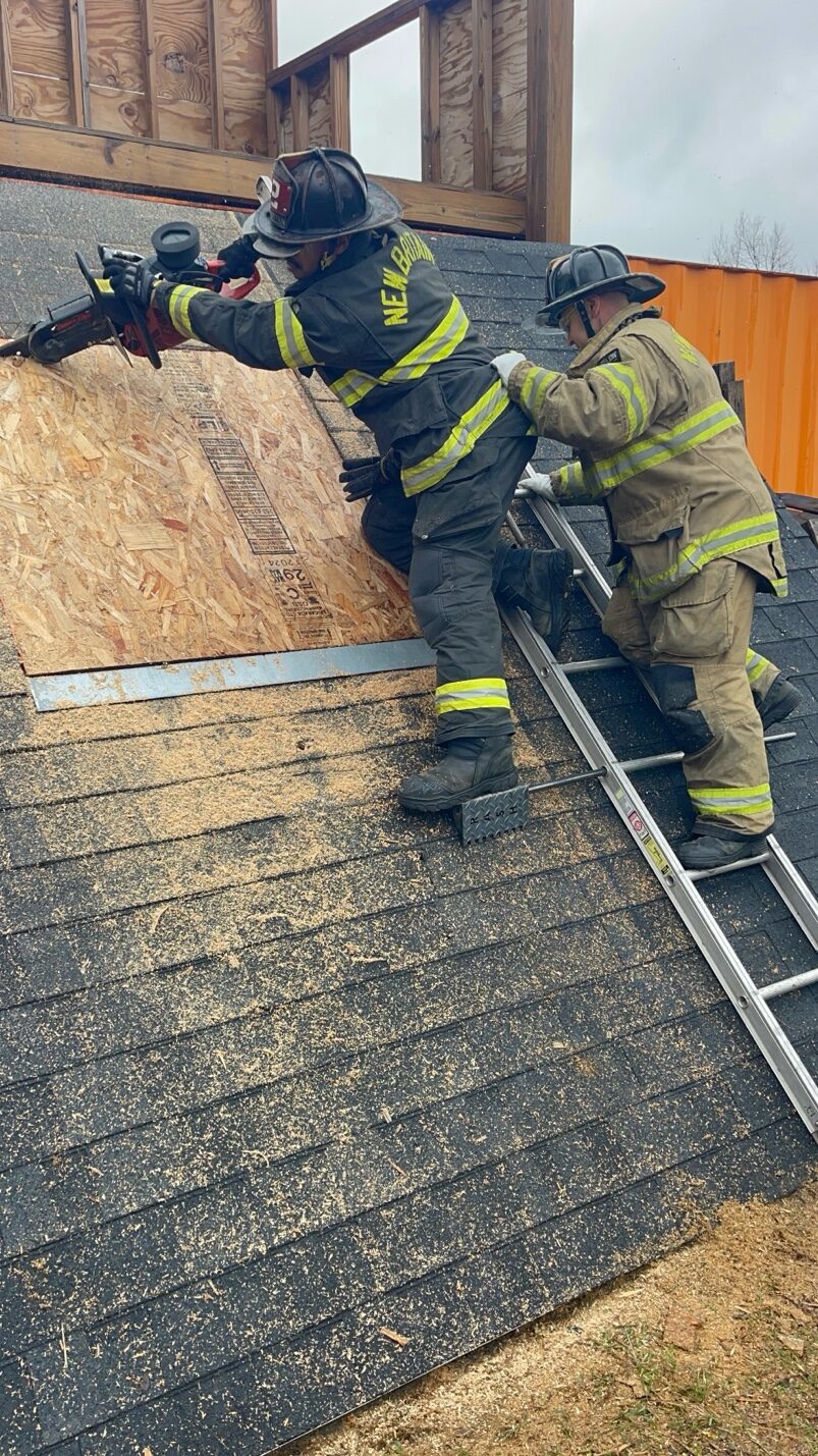 Two New Britain firefighters cutting a ventilation hole while standing on the Rash Bar during training