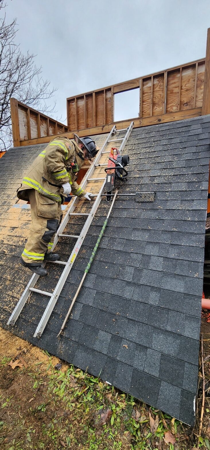 Firefighter on ladder with saw and Rash Bar deployed on training roof