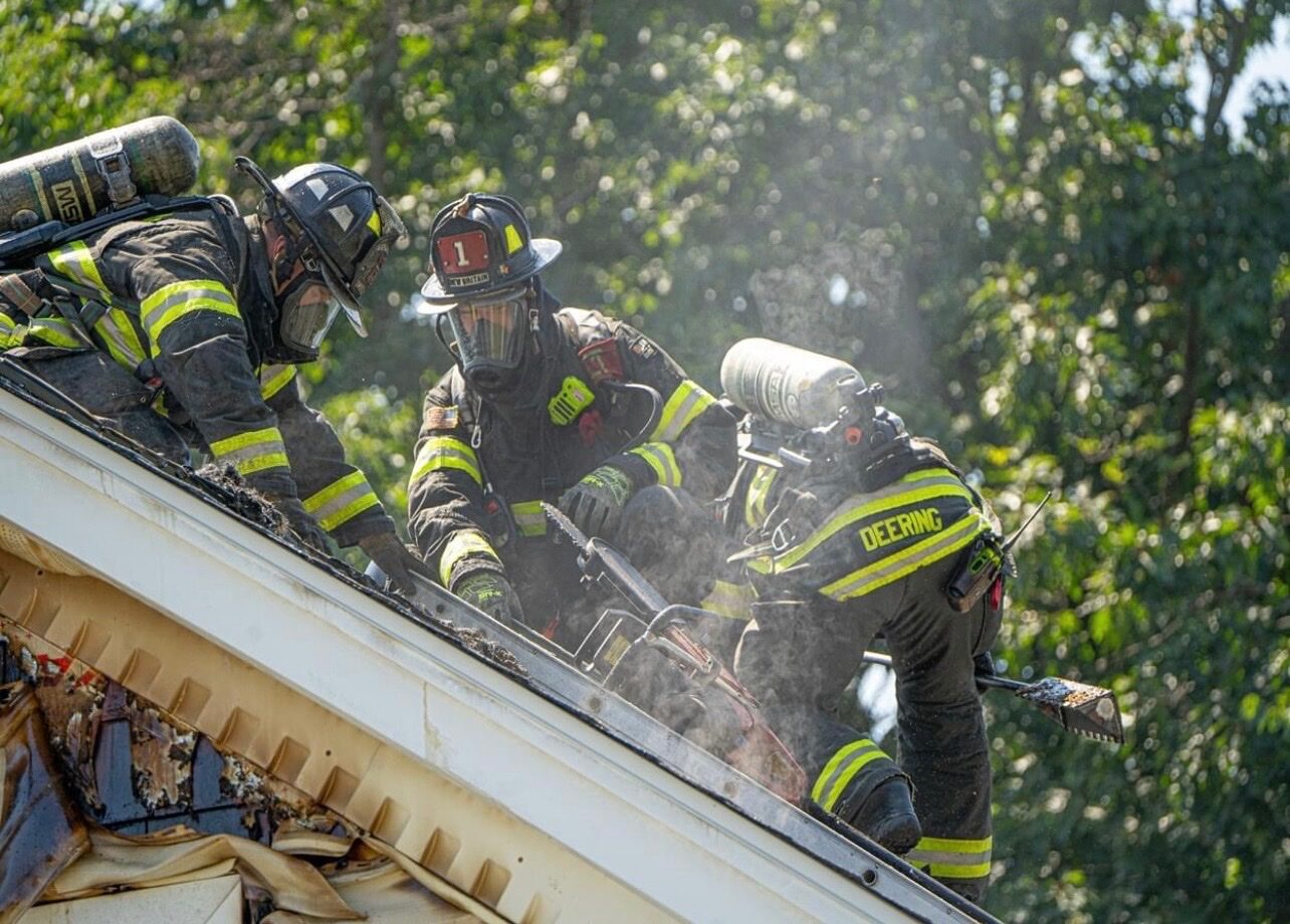 Two firefighters working on a roof at a structure fire with saws and the Rash Bar