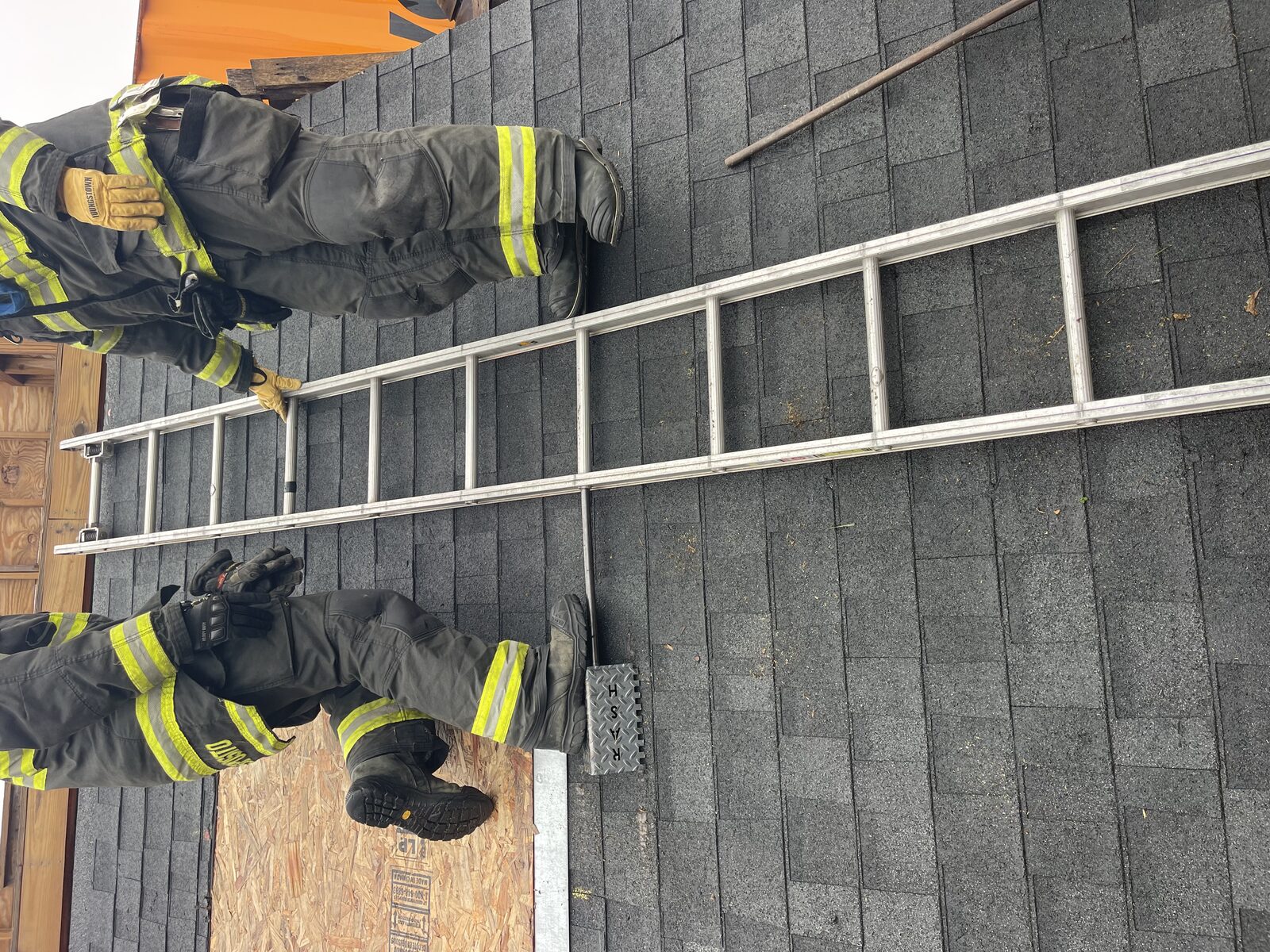 Two firefighters on a pitched roof with Rash Bar deployed under the roof ladder